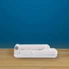 A white, foldable device sits closed on a wooden surface against a blue background. It appears compact and streamlined, with a hinge mechanism.