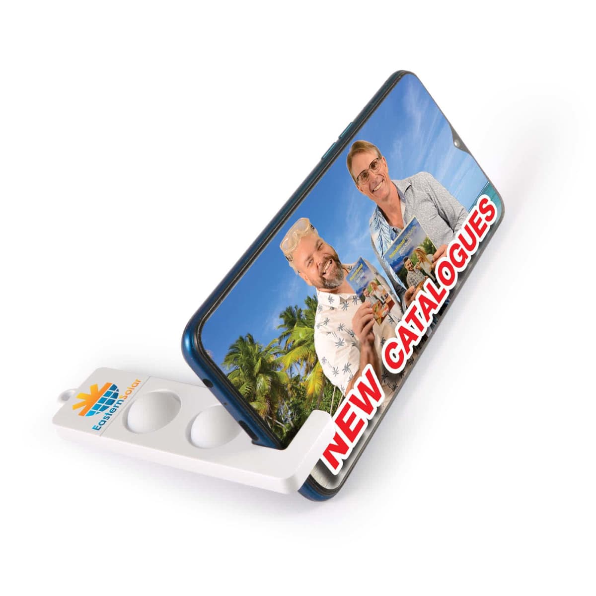A smartphone displaying two smiling people holding brochures, with a tropical background. The text NEW CATALOGUES is in bold red letters on the screen. The phone is propped up by a branded folding stand with circular cutouts.
