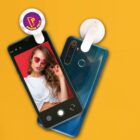 Two smartphones with lens attachments on a yellow background. The phone on the left displays a woman posing for a selfie, wearing red sunglasses and a white top. The attachment on the right phone reads Phone Pals.
