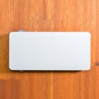 A rectangular, white wireless charging pad with rounded corners is placed on a wooden surface. The pad has a simple design and a solid color, contrasting with the warm wood grain background.