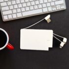 A power bank with attached charging cables is on a dark surface next to an Apple keyboard. A black cup with a red handle is partially visible.