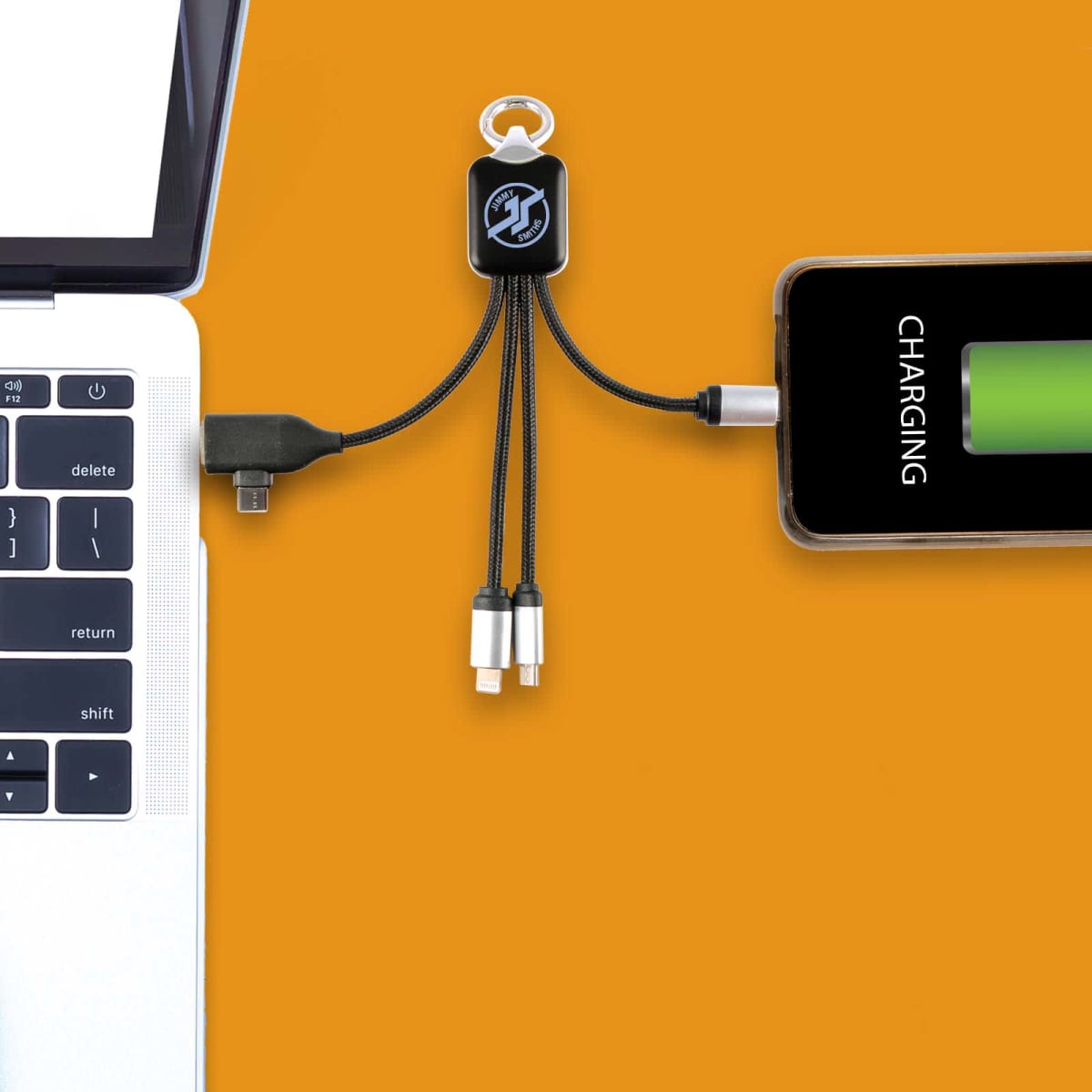 A laptop connected to a phone via a multi-device charging cable against an orange background. The cable has multiple connectors, and the phone screen displays a charging symbol with a green battery icon.