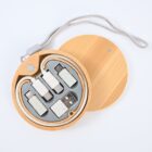 A circular bamboo case with a gray inner compartment containing various USB adapters and a coiled cable. The case has a matching bamboo lid and a looped strap attached to the side.