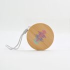 Round wooden coaster with a colorful, wave-like pattern on top. It has a gray string attached for hanging. The background is a plain, light surface.