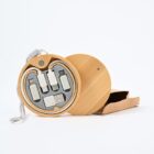 A round wooden case with a grey interior holds several white electronic adapters, including USB and Type-C connectors. The case is open, with its lid resting beside it, and a cardboard box is partially visible in the background.