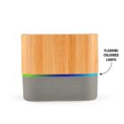 A cylindrical wooden Bluetooth speaker with a gray base featuring five control buttons. An arrow points to the base, labeled flashing coloured lights. The buttons are for play, pause, and power functions.