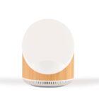 A minimalist, circular table lamp with a white front and a wooden base, featuring a slatted design on the lower section. The lamp projects light forward, blending modern and natural elements.