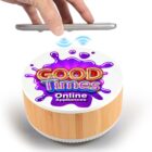 A hand holding a smartphone above a round device with a wooden base and white top. The top features colorful text reading GOOD Times and Online Appliances, with a purple splash design and a Wi-Fi symbol above it.