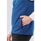 A person in a blue vest puts their hand into a side pocket.