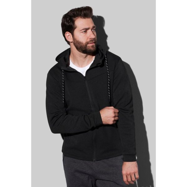 Man in a black hoodie looks to the side against a gray background.