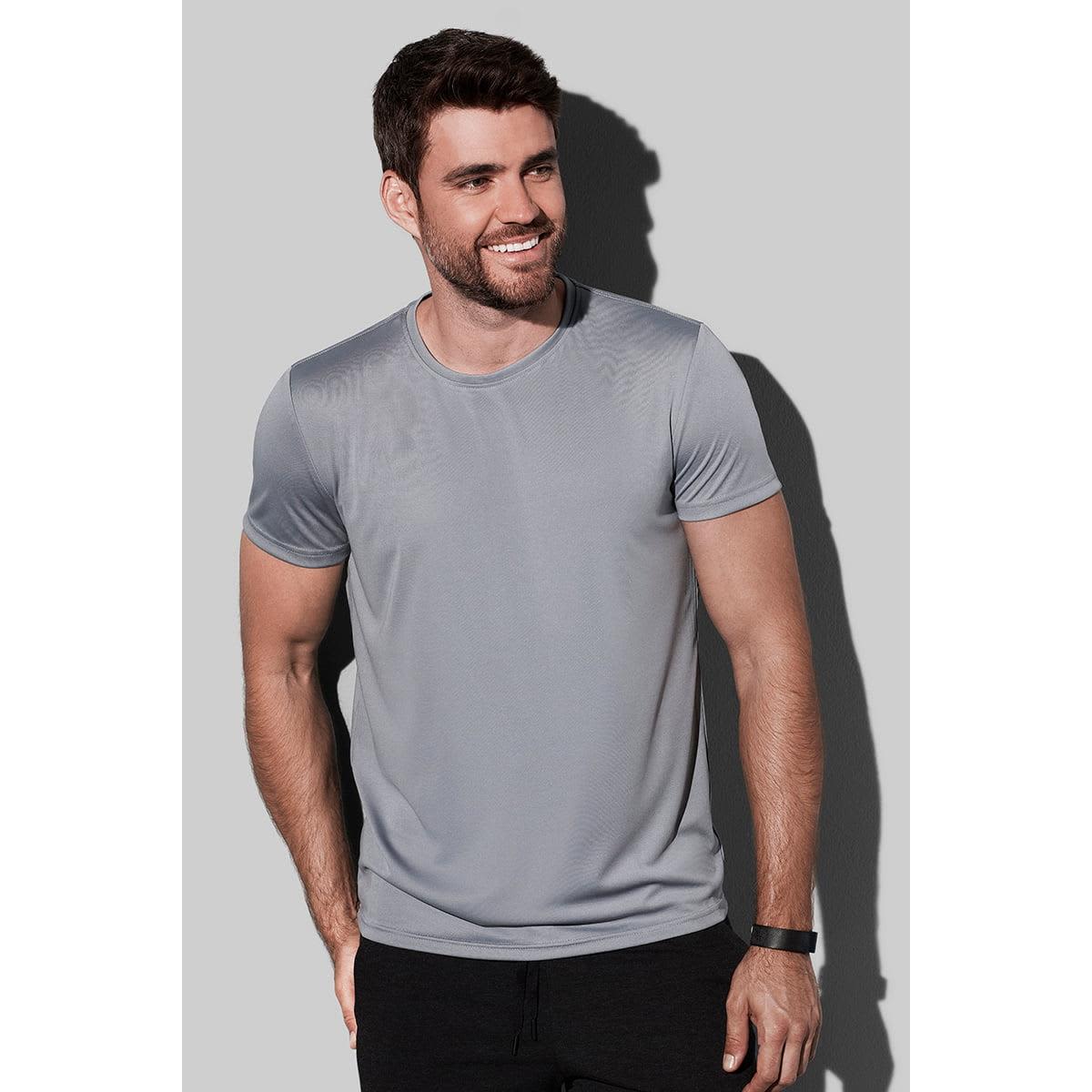 Man in a gray t-shirt and black pants smiling against a gray background.