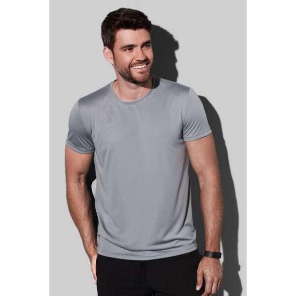 Man in a gray t-shirt standing against a gray background, smiling.