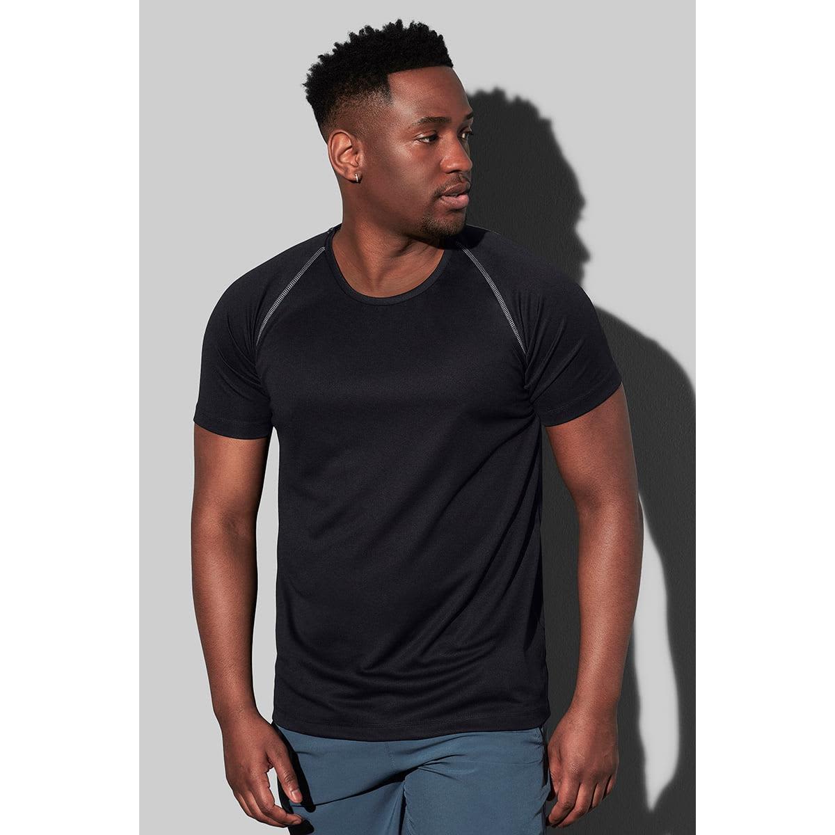 Man in a black T-shirt and blue shorts stands against a gray background.