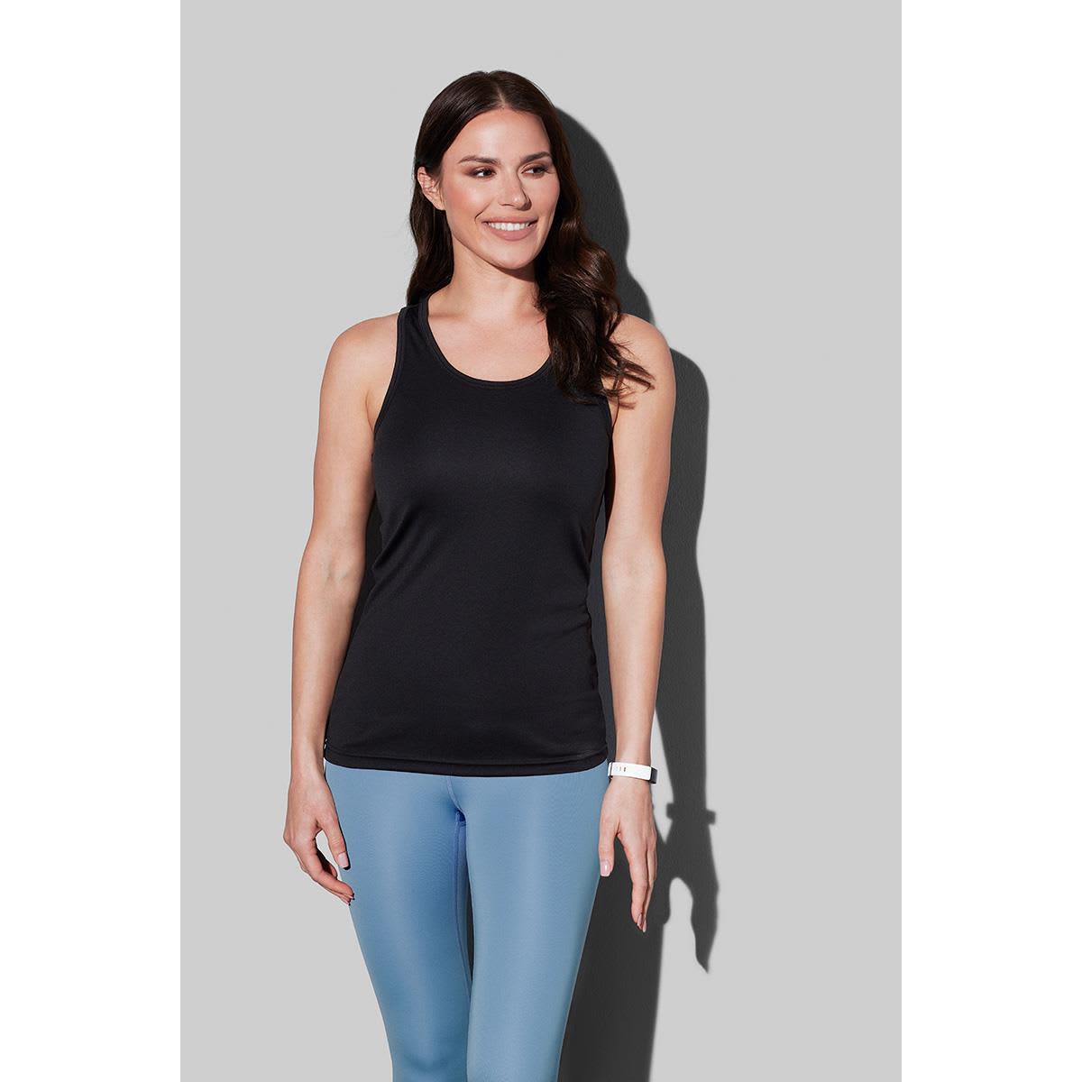 Woman in black tank top and blue leggings smiling against gray background.