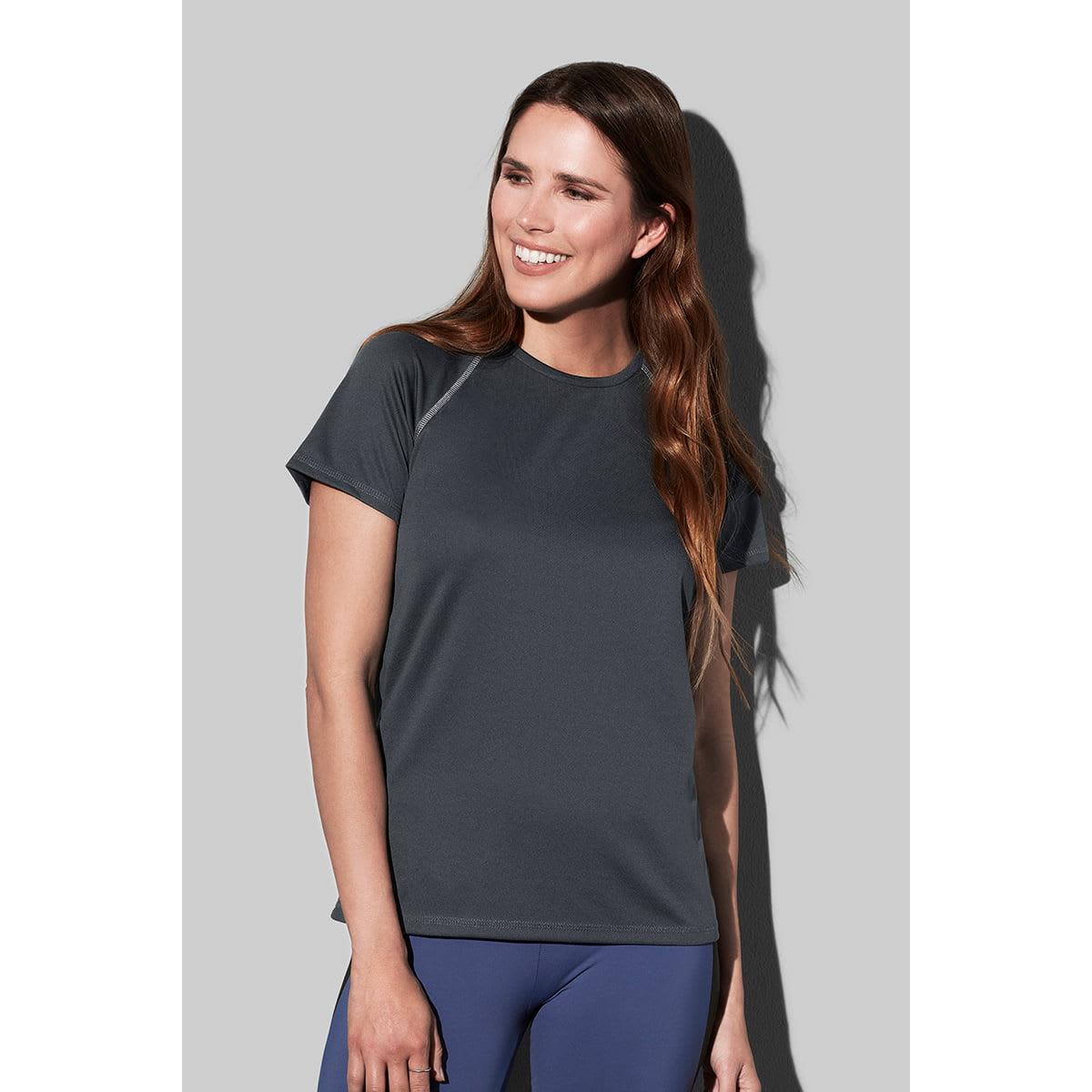 Smiling woman with long hair wearing a dark gray shirt and blue leggings.