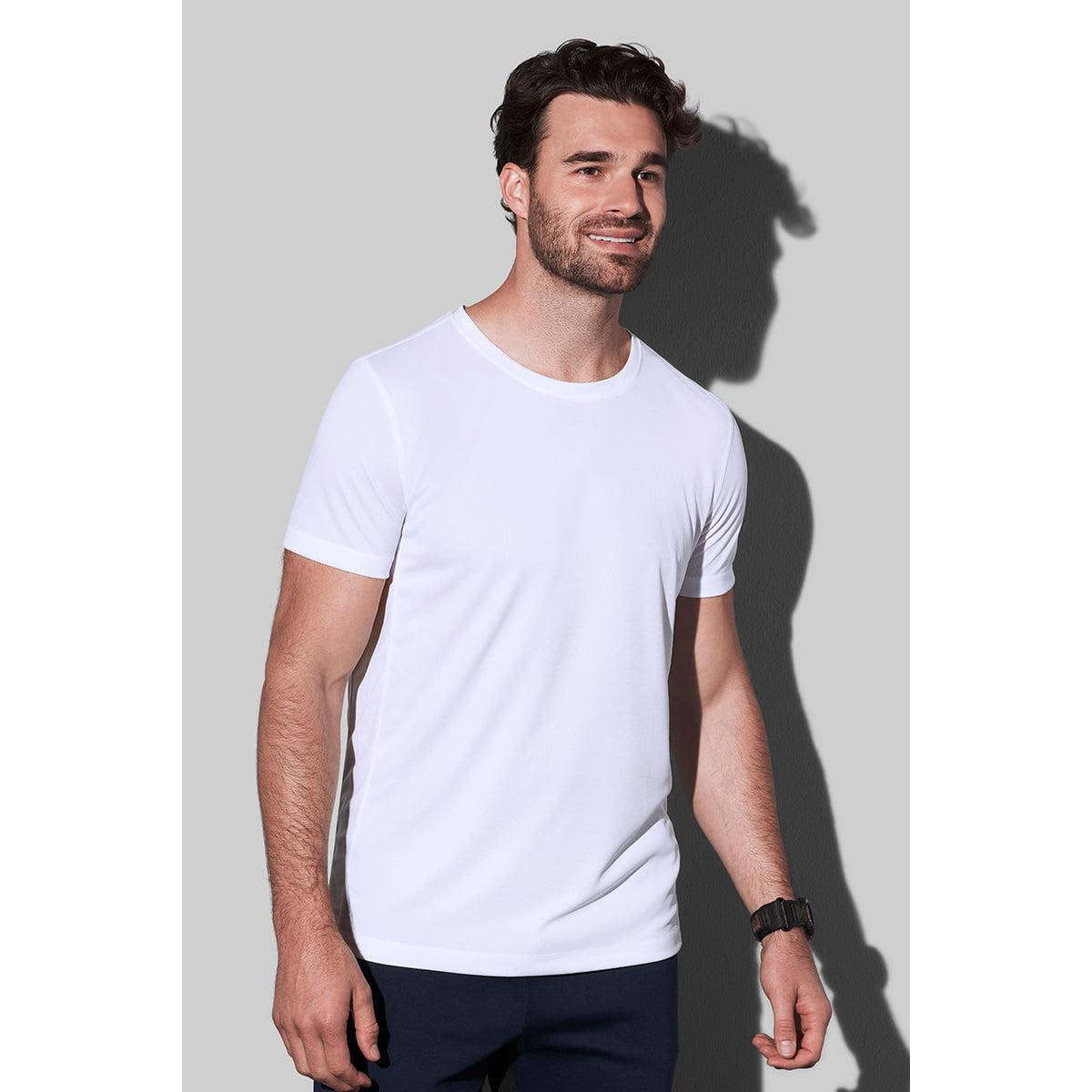 Man in a white t-shirt and dark pants smiling against a gray background.