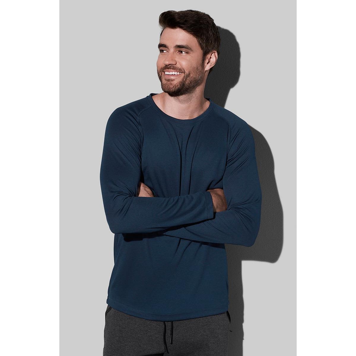 Man in a blue long-sleeve shirt, arms crossed, smiling against a gray background.