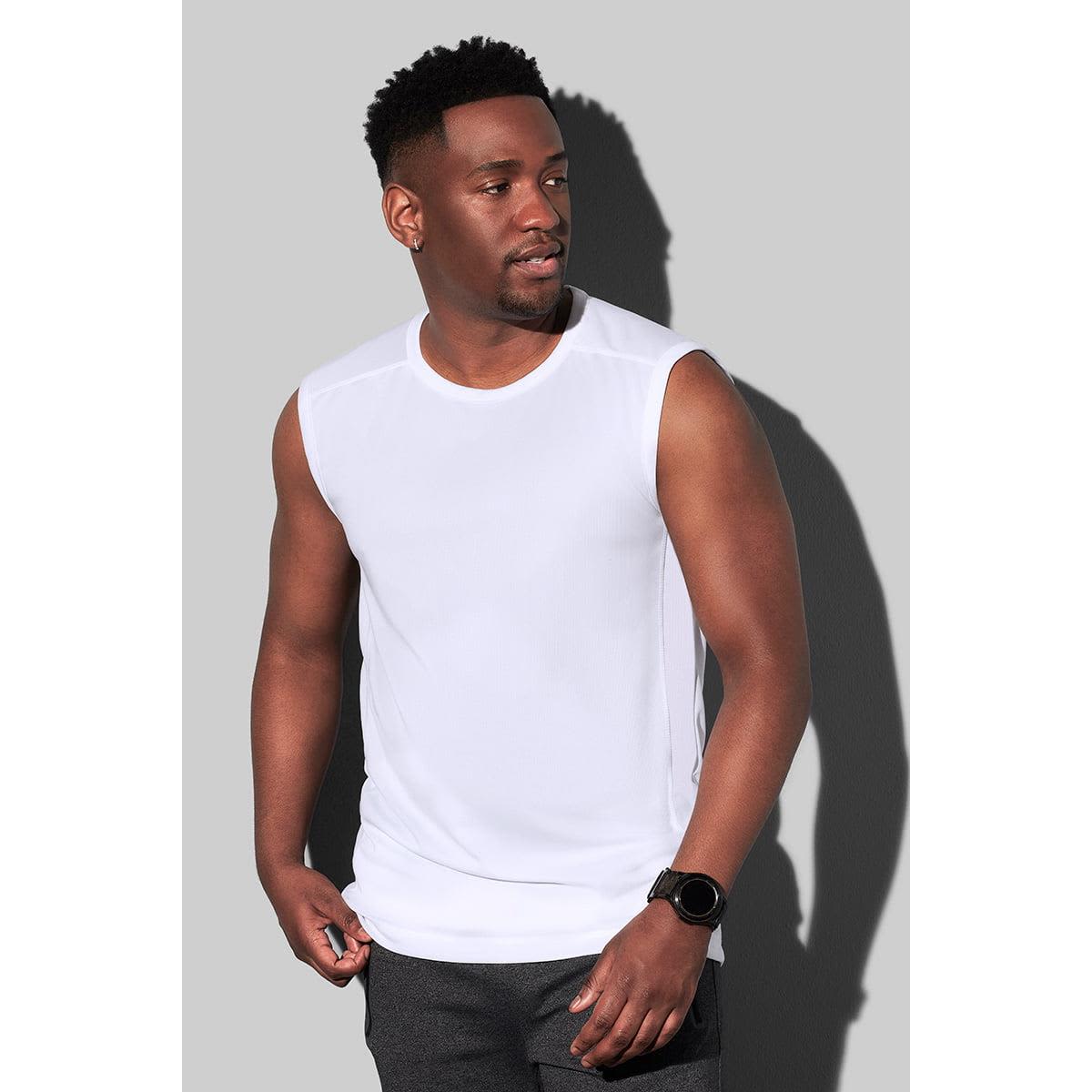 Man wearing a white sleeveless shirt and dark pants against a gray background.