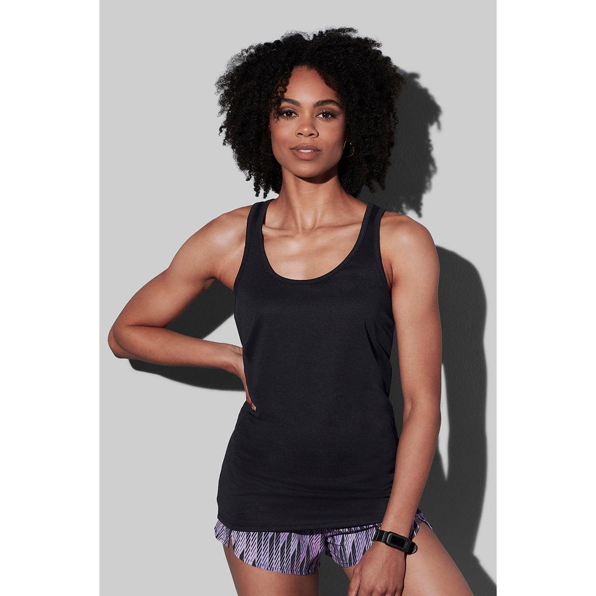 Person in black tank top and patterned shorts standing against a gray background.