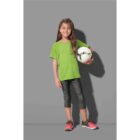 Girl in green shirt and leggings holding a soccer ball, smiling against a gray background.
