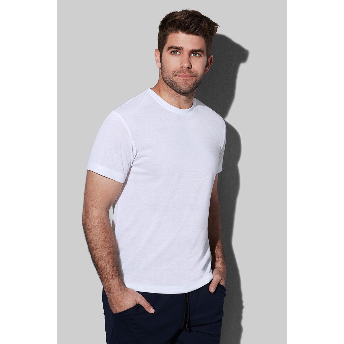 Man in a white T-shirt and blue pants standing against a gray background.