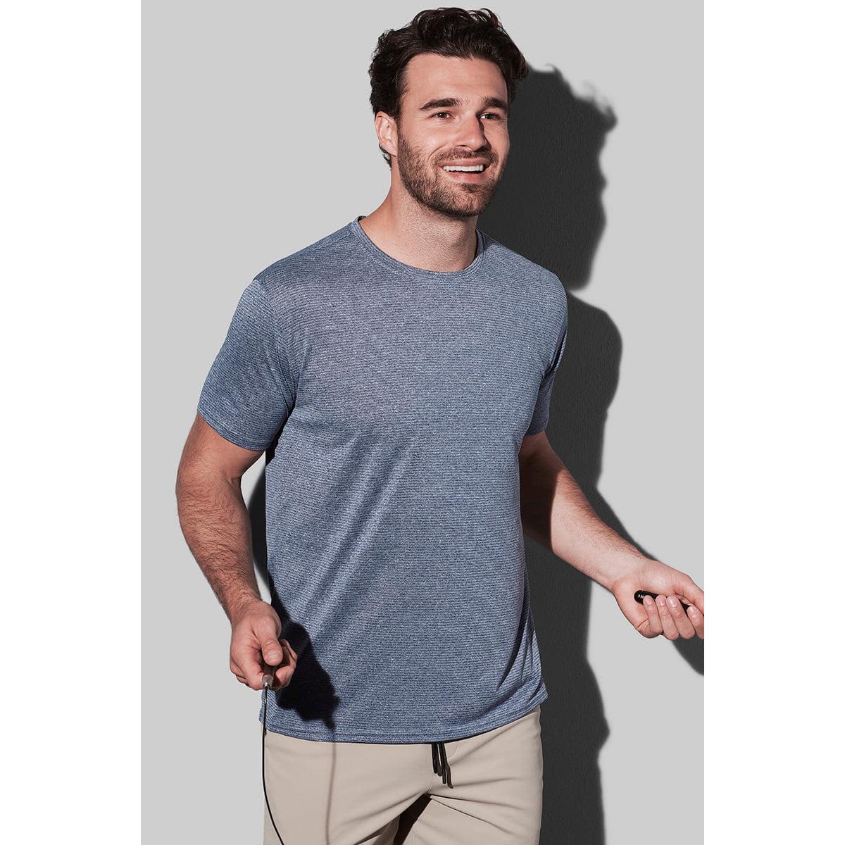 Man in gray T-shirt and beige pants smiling, holding a jump rope.