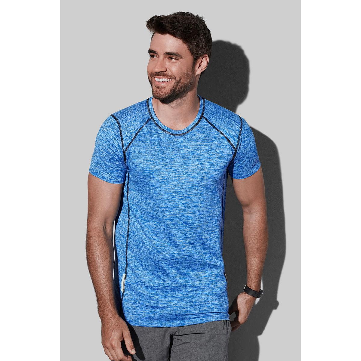 Man in a blue athletic shirt smiling against a gray background.