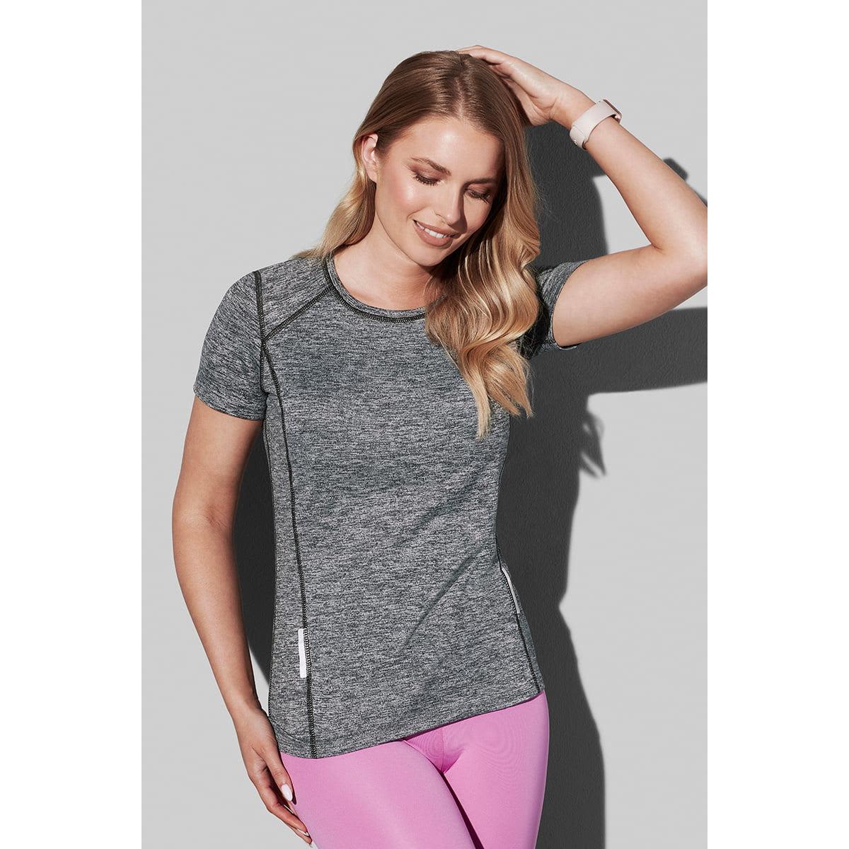 Woman in gray athletic shirt and pink leggings smiles, posing against a plain background.