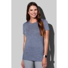 Woman in blue shirt smiles, standing against a gray background.