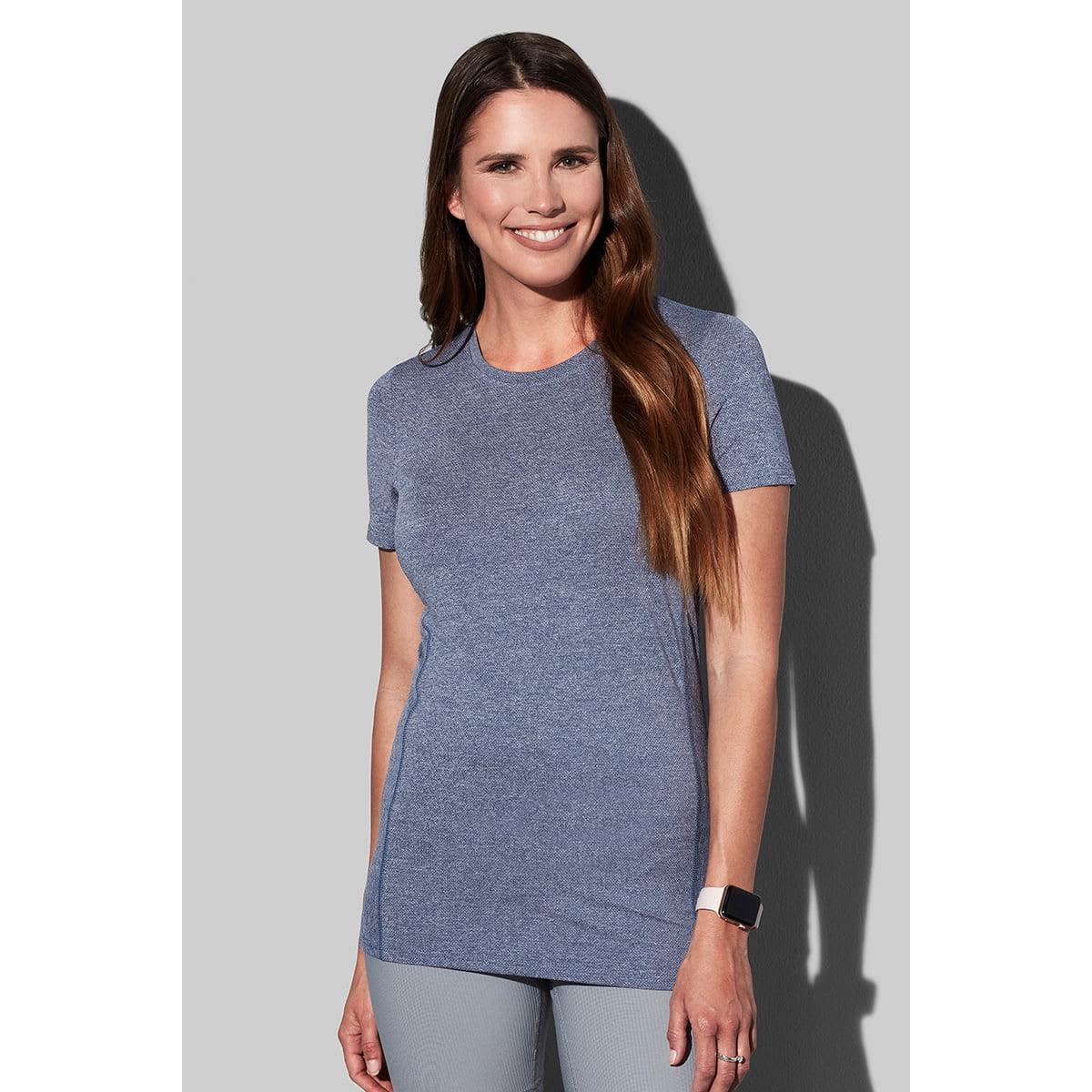 Woman in blue shirt smiles, standing against a gray background.