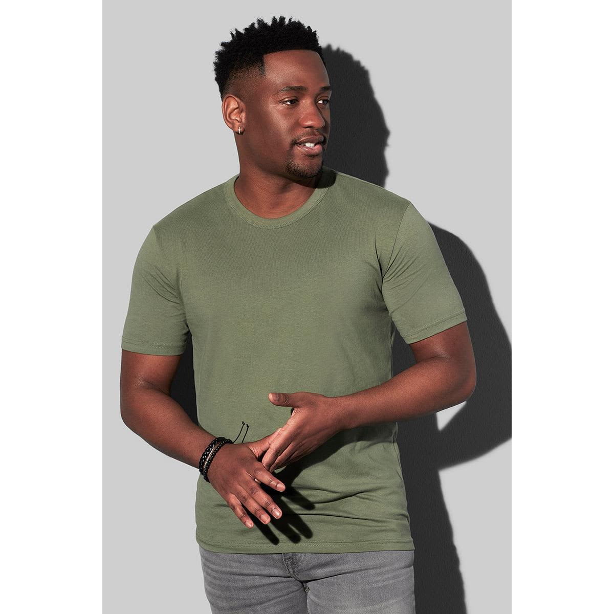 Man in green T-shirt and jeans against gray background, looking to his right.