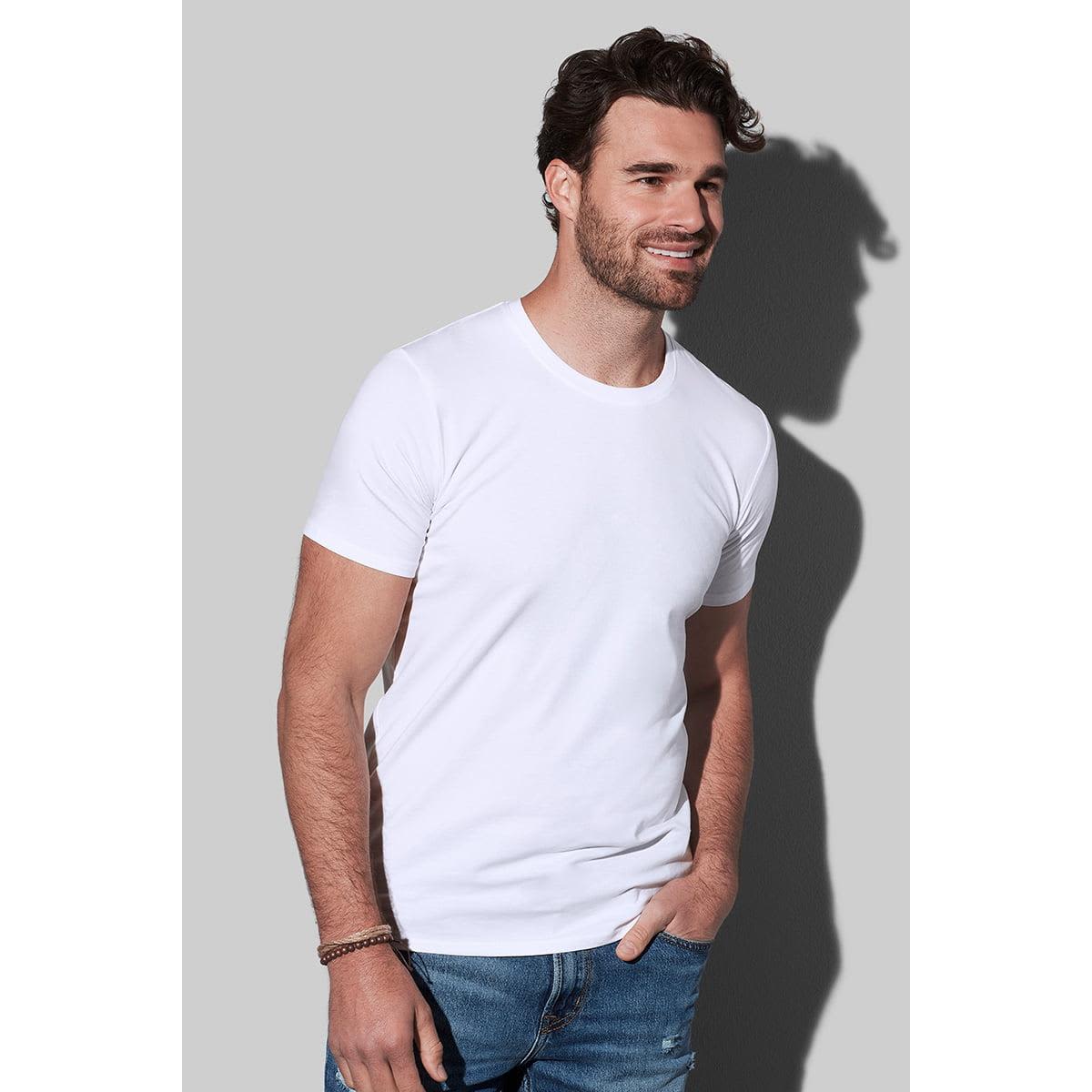 Man in a white t-shirt and jeans smiling against a gray background.