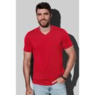 Man in a red T-shirt and jeans smiles against a gray background.