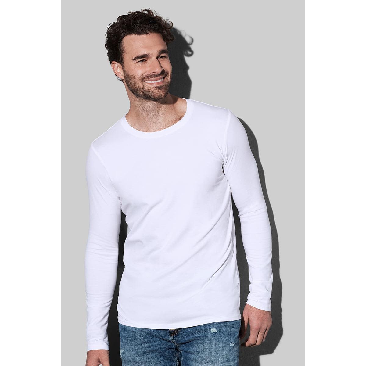 Man in a white long-sleeve shirt and jeans, smiling against a gray background.