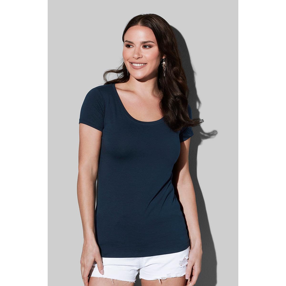 Smiling woman in a navy T-shirt and white shorts, against a gray background.