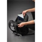 Person placing a tablet into a black backpack on a dark surface.