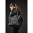 Woman with ponytail carrying a large black duffel bag over her shoulder.