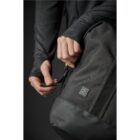 Person adjusting a strap on a black backpack with a logo, wearing a dark sweater.