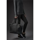 Person in dark workout clothes carrying a large black duffel bag.