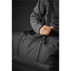 Person holding a large black duffel bag with a shoulder strap, wearing a dark jacket.