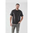 Man in a dark polo shirt and jeans smiling against a white background.