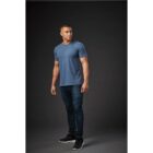 Man in blue t-shirt and jeans standing in a studio against a dark background.