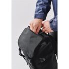Person zipping a black backpack wearing a blue shirt.