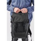 Person in a blue jacket holding a black backpack against a plain background.