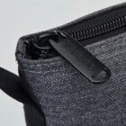 Close-up of a black zipper pull labeled Hirano on a textured gray fabric bag.