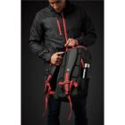 Person in black jacket holding a backpack with red straps and a water bottle.