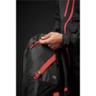 Person adjusting straps on a black and red backpack against a dark background.