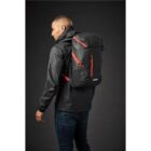 A person in a black jacket modeling a black backpack with red accents.