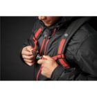 Person wearing a black jacket buckling a red backpack strap.
