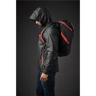 Person in black jacket with red zippers, wearing a hood, carries a black backpack with red straps.